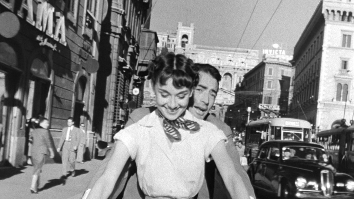 Audrey_Hepburn_and_Gregory_Peck_on_Vespa_in_Roman_Holiday_trailer